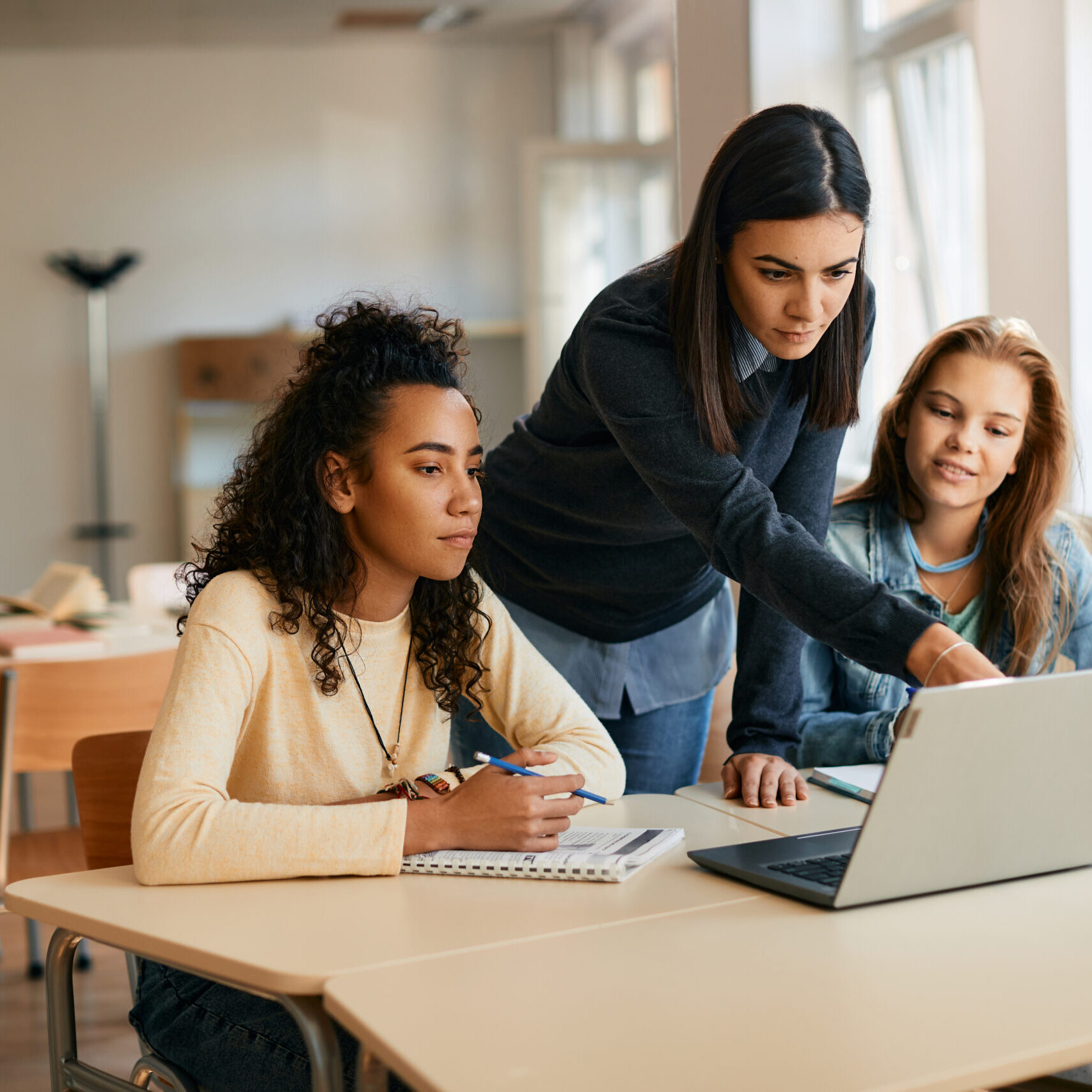 High school professor assists her students in e-learning on laptop in classroom.